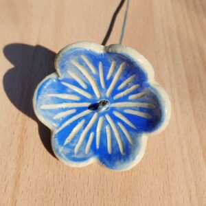 fleur en céramique montée sur tige. Fond couleur lavande, avec nervures gravées