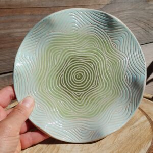 assiette décorative ondulée en céramique. Poterie colorée en dégradé de bleu et vert, avec motif de lignes gravées évoquant les mouvements de l'eau